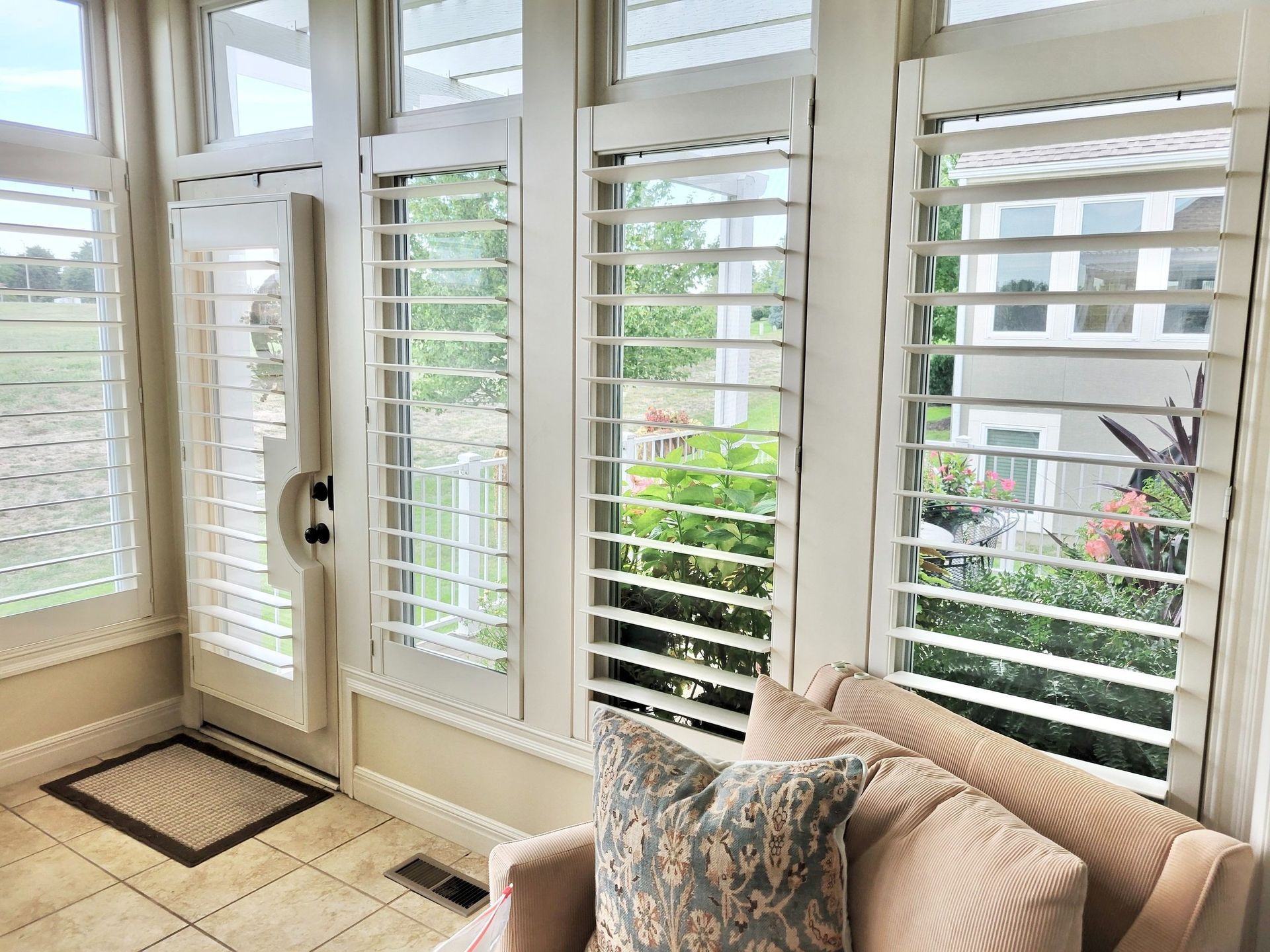 Sunroom with white shutters, a peach couch, and an outdoor view.
