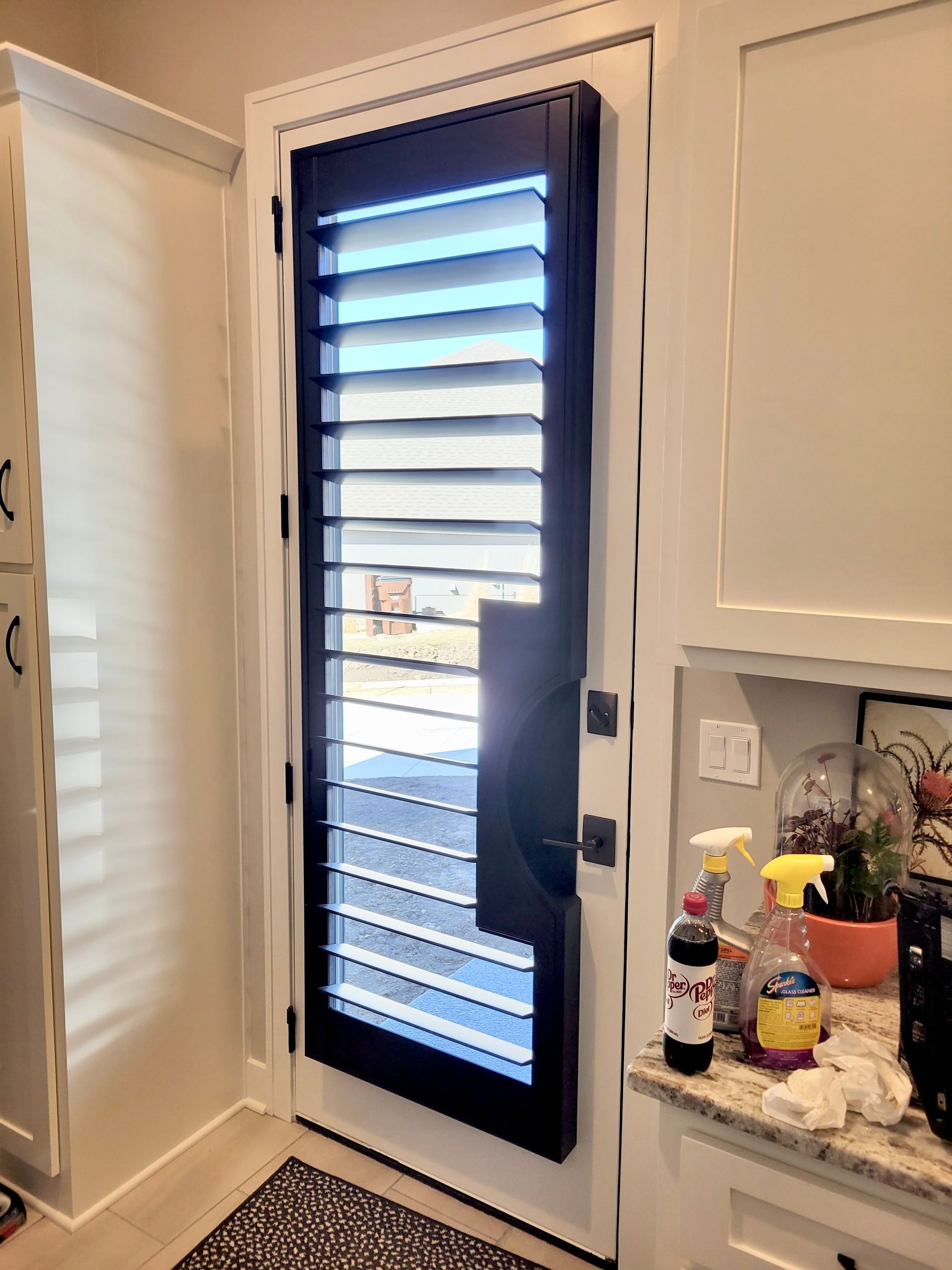 A dark door with horizontal slats. The door has a long handle and is surrounded by white cabinets.