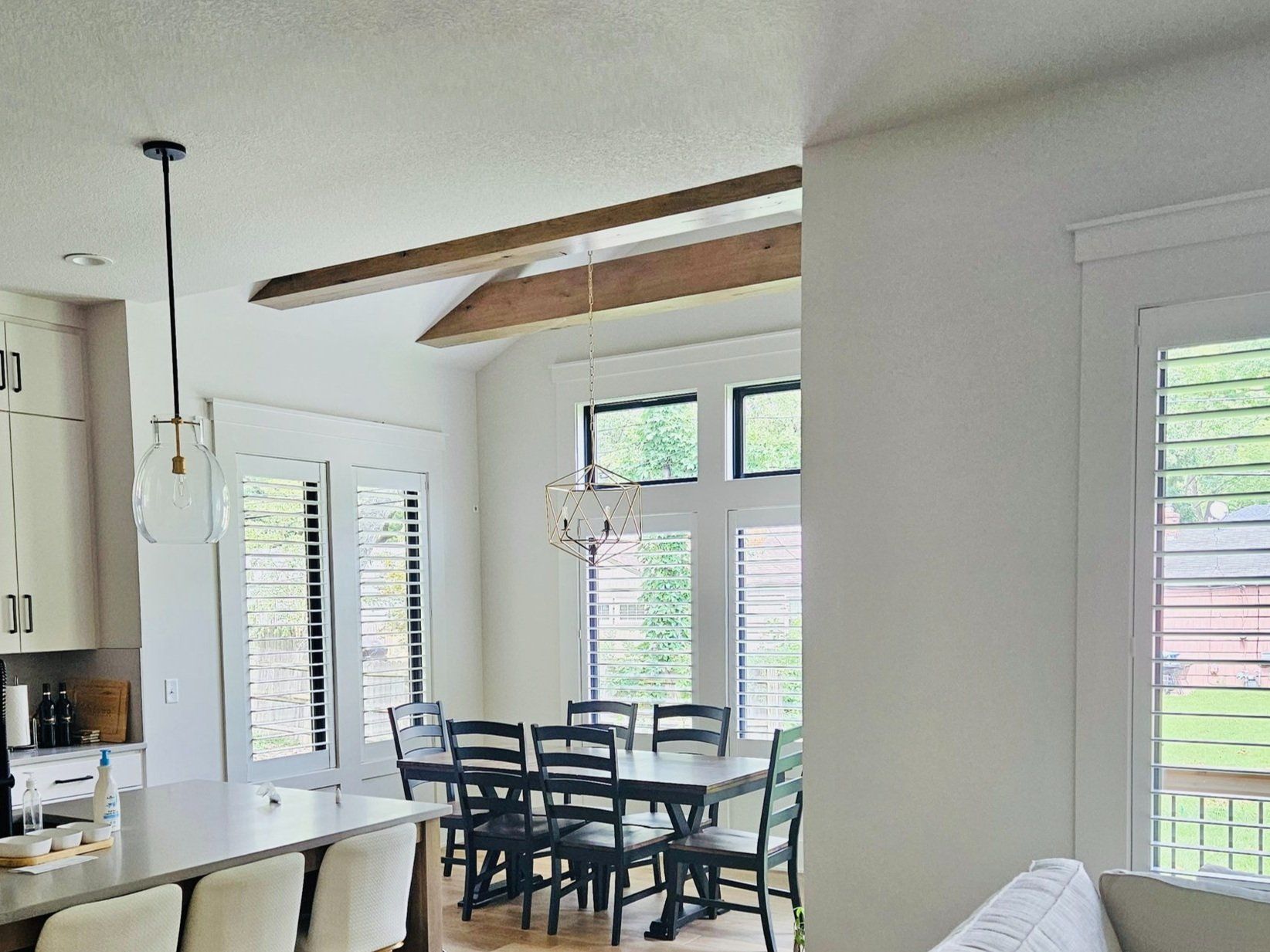 Dining room with a long table, black chairs, and white shutters.