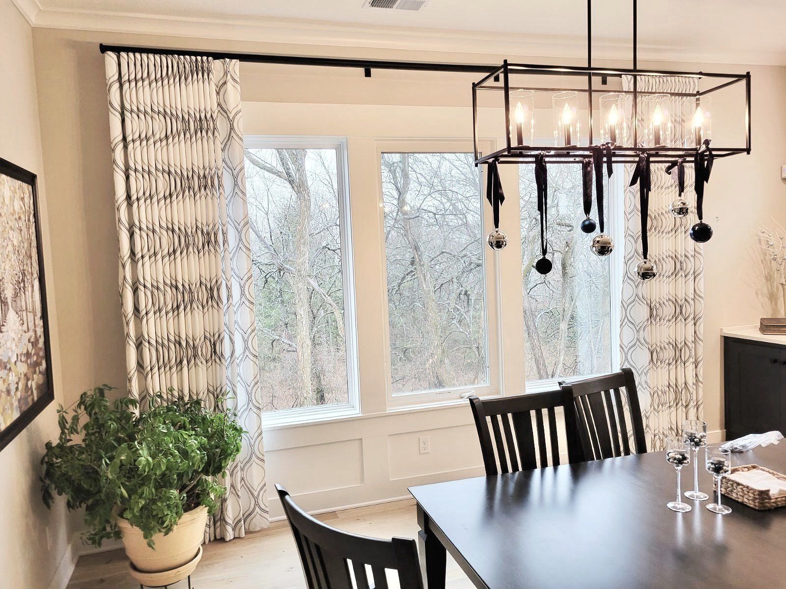 Dining room with windows, dark table and chairs, chandelier, and patterned curtains.