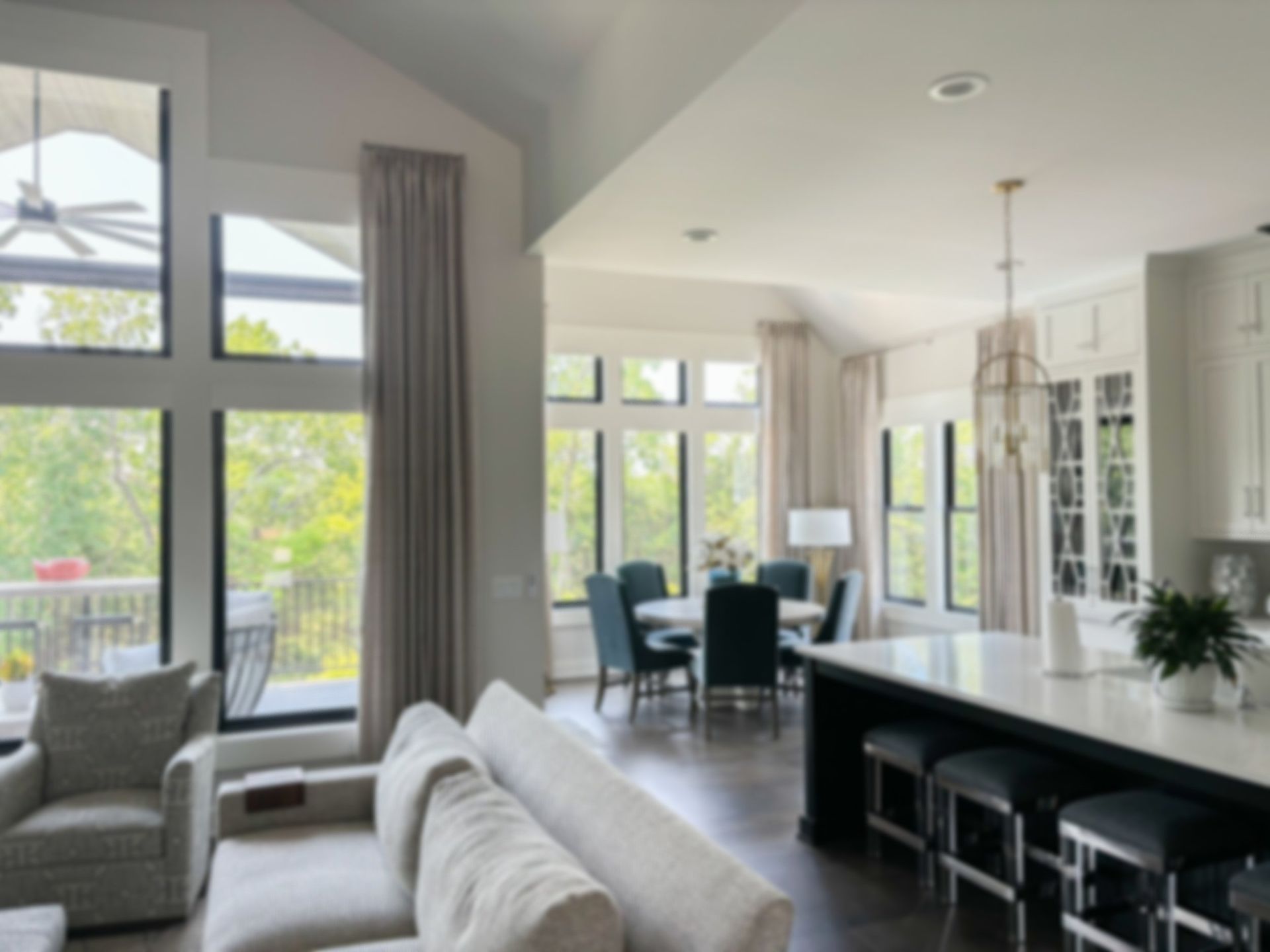 Living room with tall windows, dark island, and a dining area, featuring neutral colors and natural light.