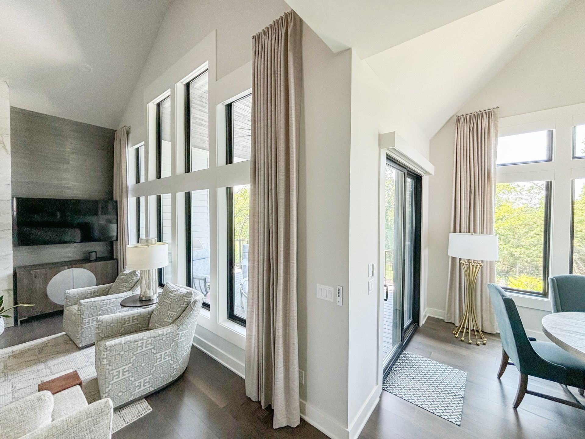 Living room with tall windows, curtains, chairs, TV, and dining area.
