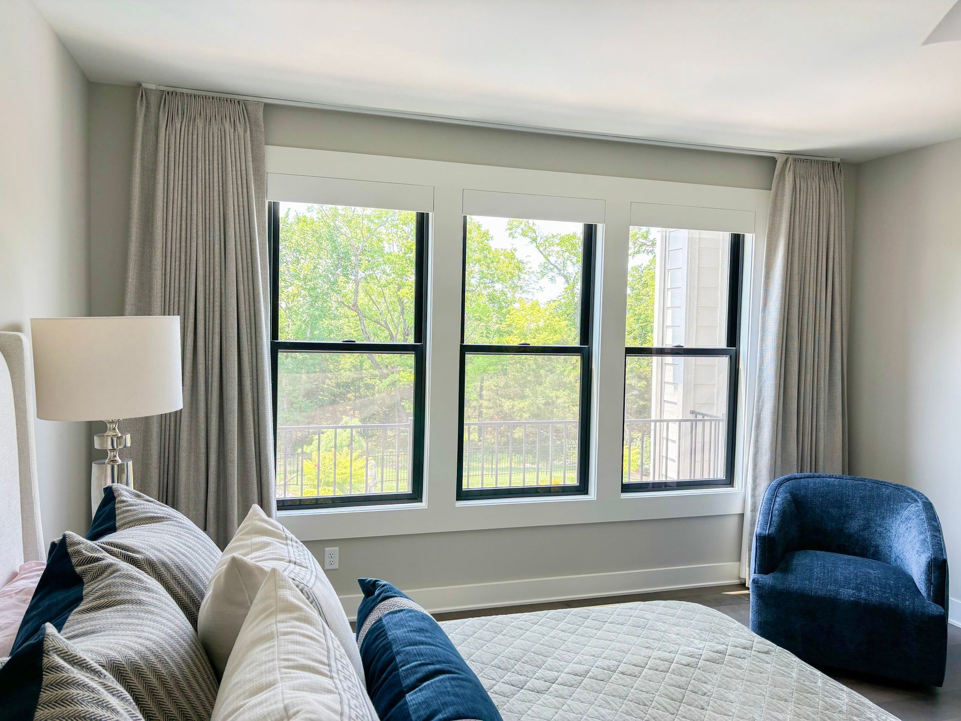 Bedroom with a triple window, gray curtains, and a blue armchair.