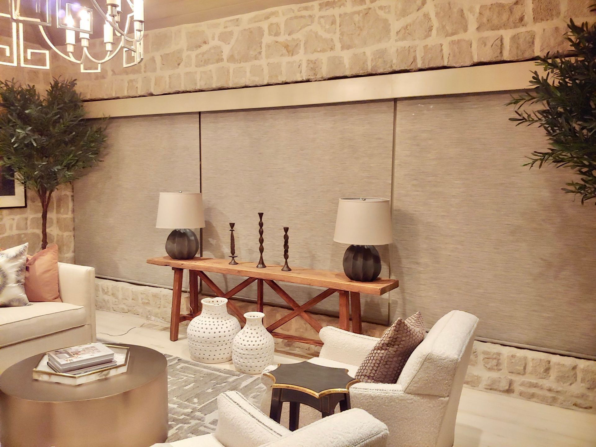 Living room with stone wall, wooden bench with lamps and candles, white sofas, and round coffee table.