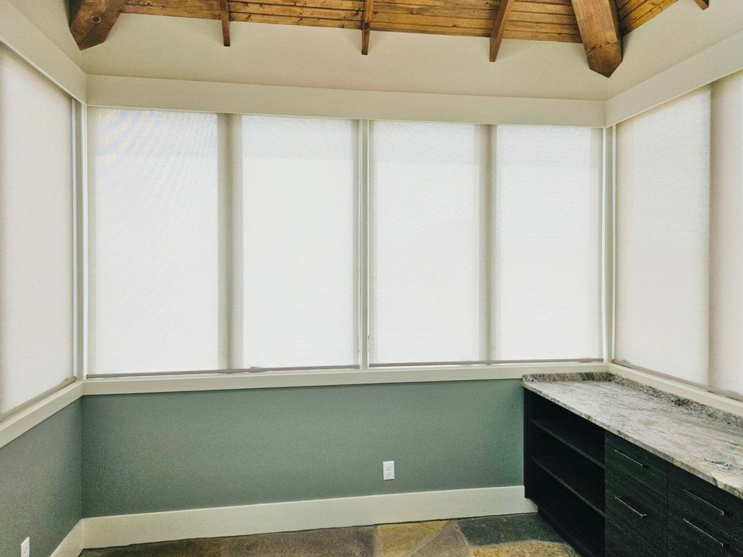 Sunroom interior with white blinds, a gray-green wall, stone floor, and dark cabinet.