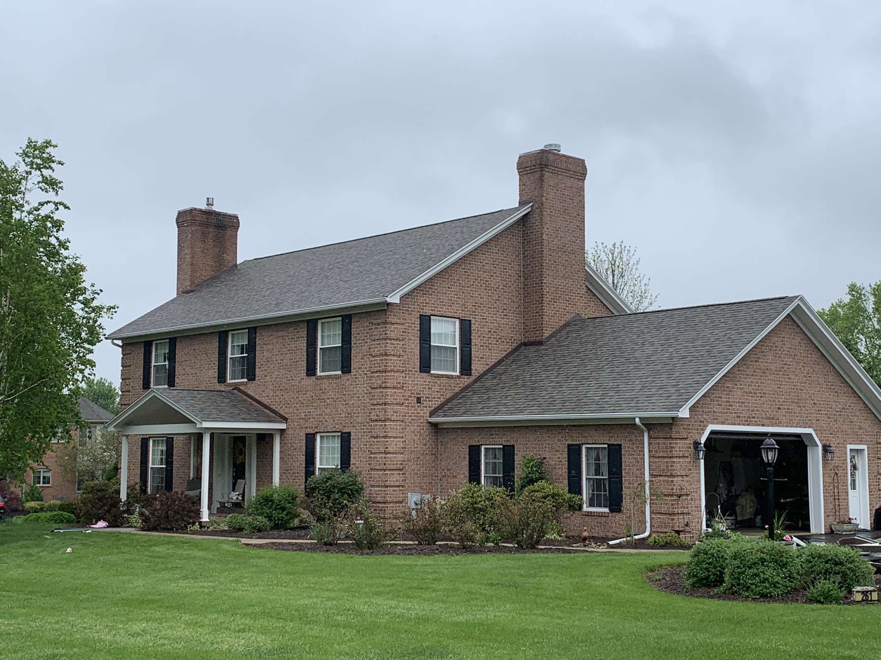 A large brick house with a gray roof and black shutters is sitting on top of a lush green field.