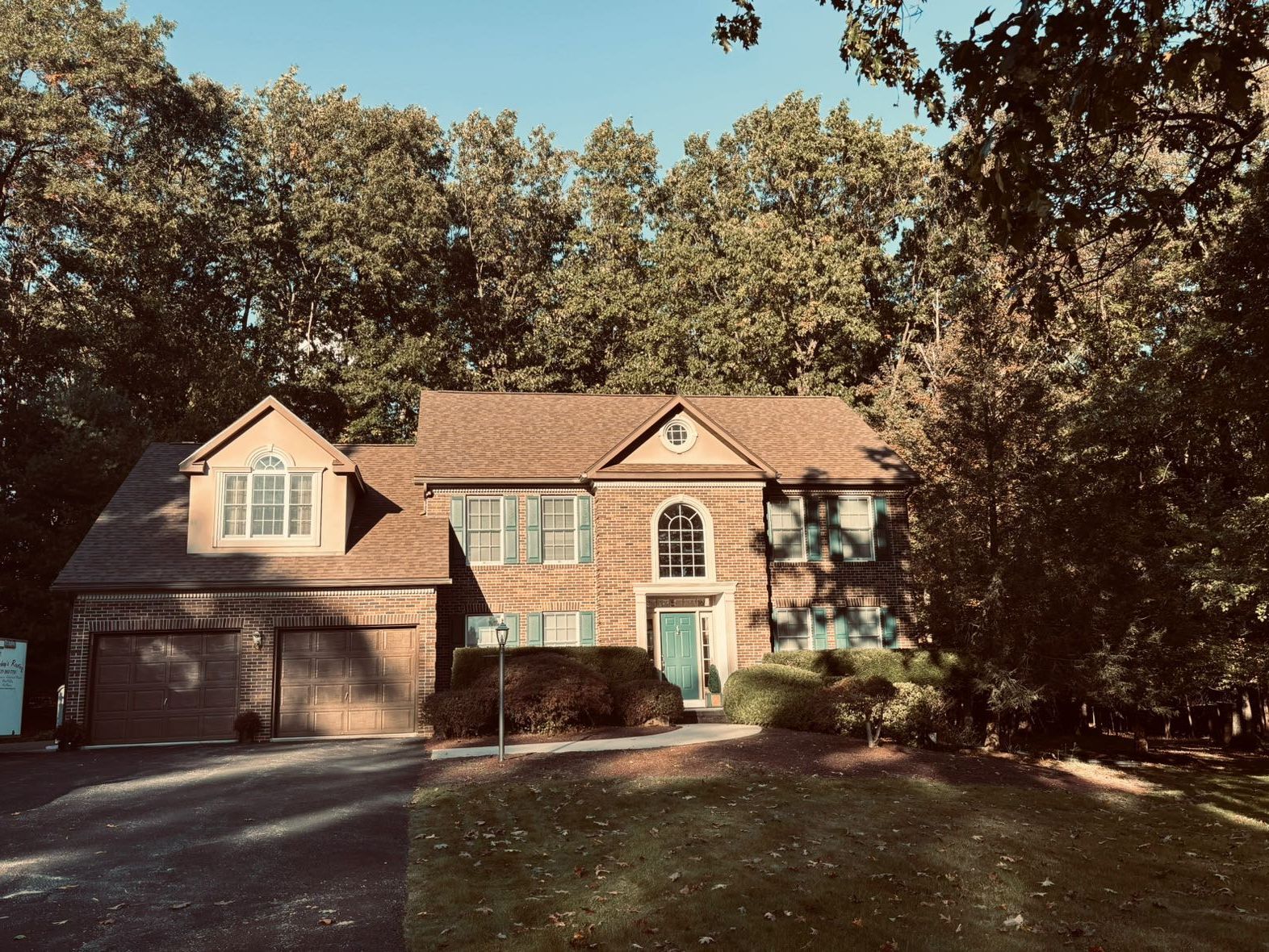 A large brick house with a brown roof is surrounded by trees