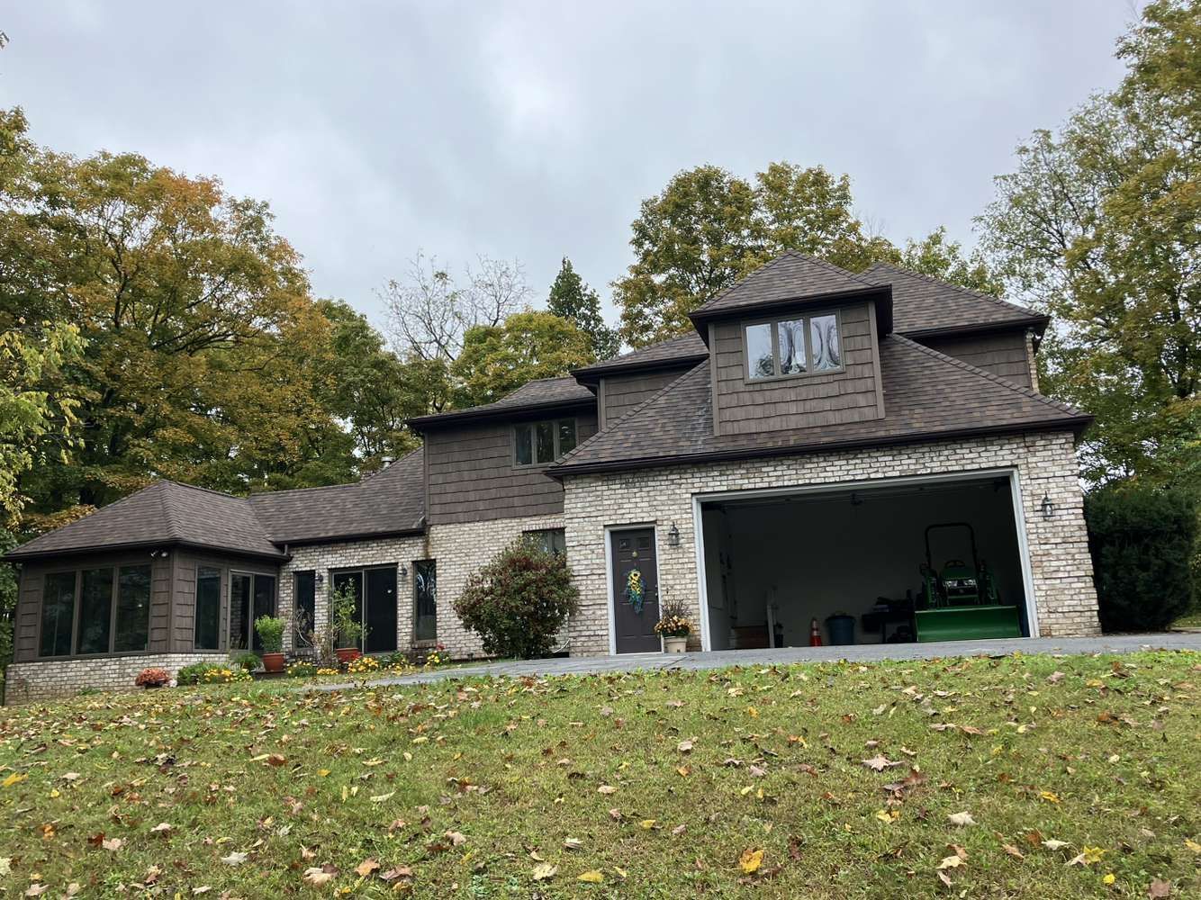 A large house with a garage is sitting on top of a lush green hill.