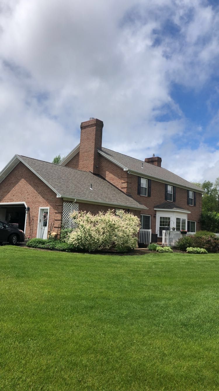 A large brick house with a gray roof is sitting on top of a lush green lawn.