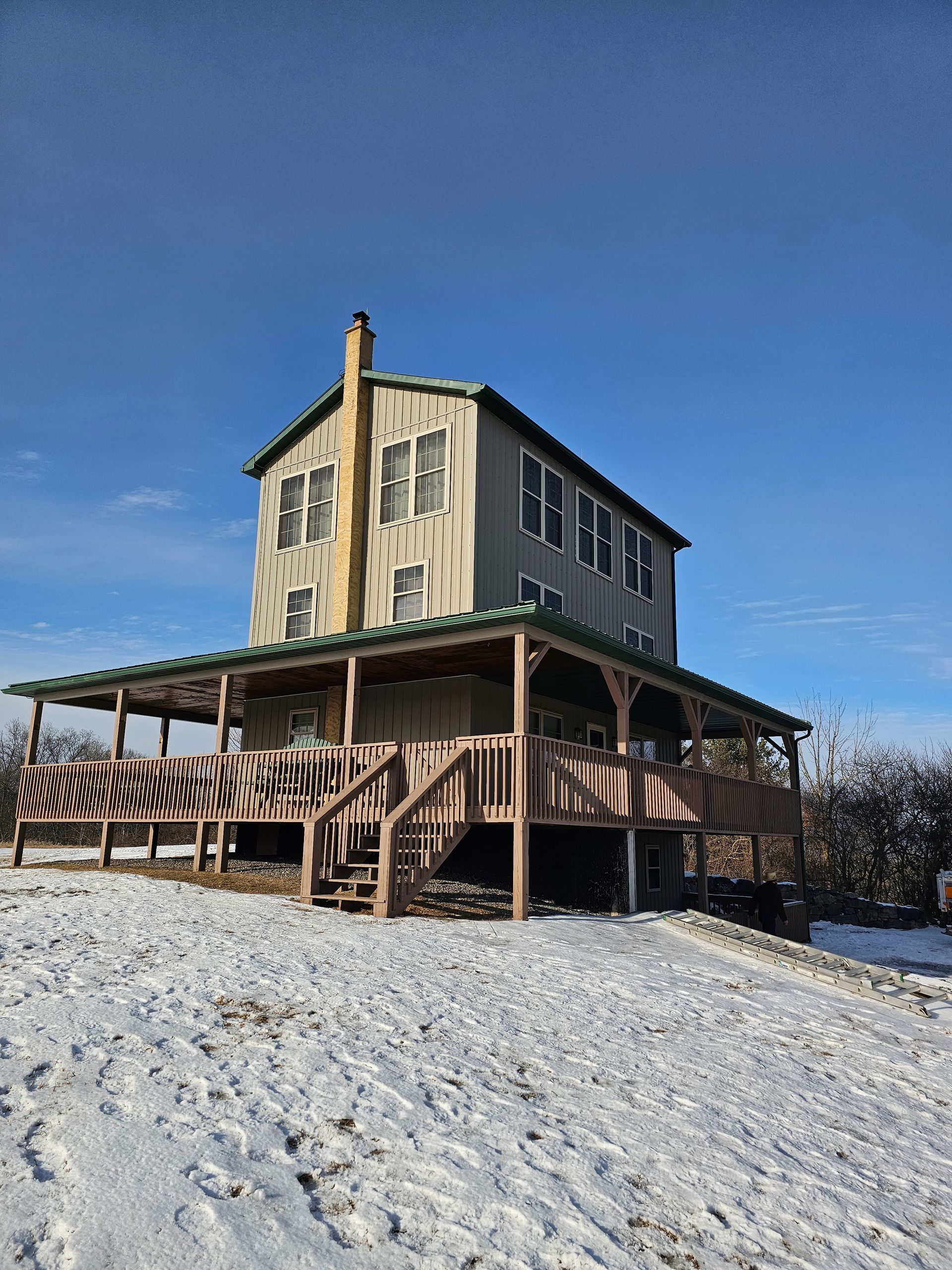 A large house with a green roof is sitting on top of a snow covered hill.