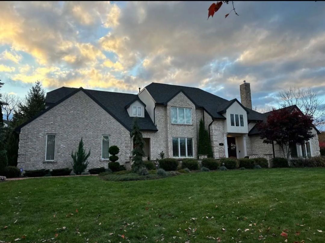 A large brick house with a black roof is sitting on top of a lush green lawn.