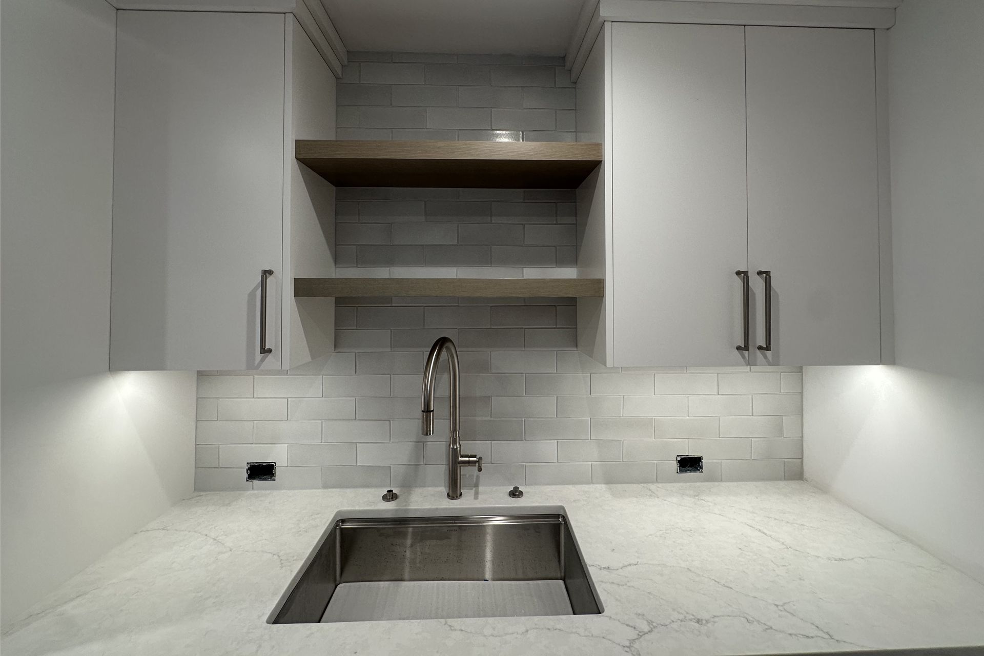 Modern white kitchen with farmhouse sink, marble counters, gray tile backsplash, and open shelves