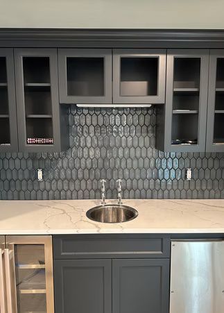 Dark gray kitchen cabinets with glass fronts, mosaic tile backsplash, and a stainless sink on a light countertop