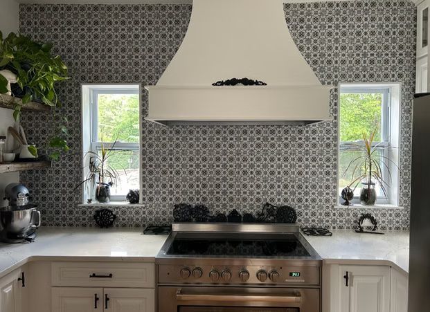 Patterned kitchen with white cabinets, stainless stove, and two windows flanking a range hood