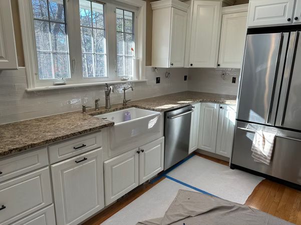Bright white kitchen with farmhouse sink, stainless refrigerator, and granite countertops
