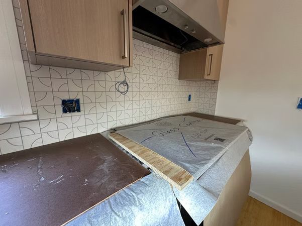 Kitchen with damaged countertop and unfinished backsplash under wooden cabinets