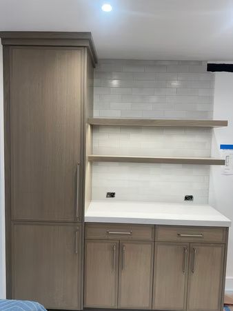 Built-in kitchen cabinets with wood finish, white tile backsplash, and open shelves under a recessed light