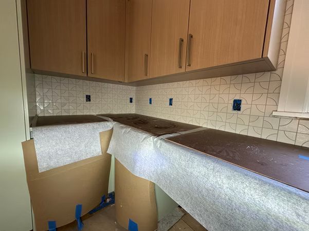 Kitchen counters wrapped in protective paper and blue tape during renovation under wood cabinets