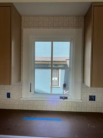 Empty kitchen with brown countertop, white window, and wooden cabinets.