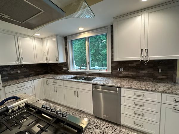 Modern kitchen with white cabinets, granite countertops, dark backsplash, and a window over the sink.