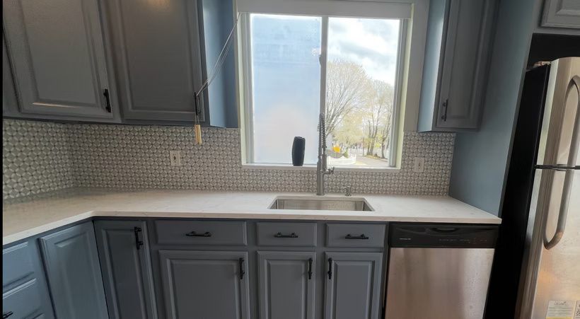 Modern kitchen with gray cabinets, white countertops, mosaic backsplash, and a window over the sink.