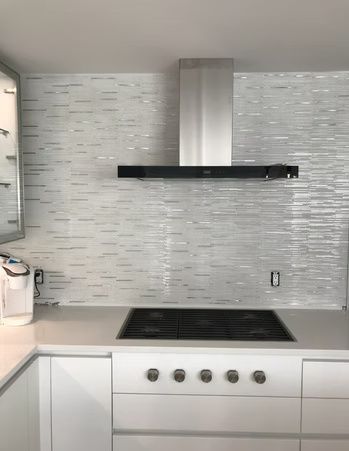 Modern white kitchen with stainless range hood, black cooktop, and light tile backsplash