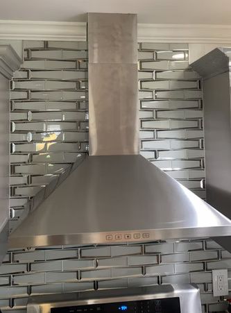 Stainless steel range hood against a gray brick-tile kitchen backsplash