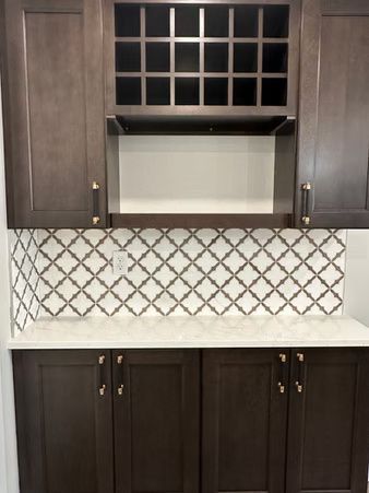 Dark wood kitchen cabinets with white countertops and patterned backsplash under a glass-front upper cabinet