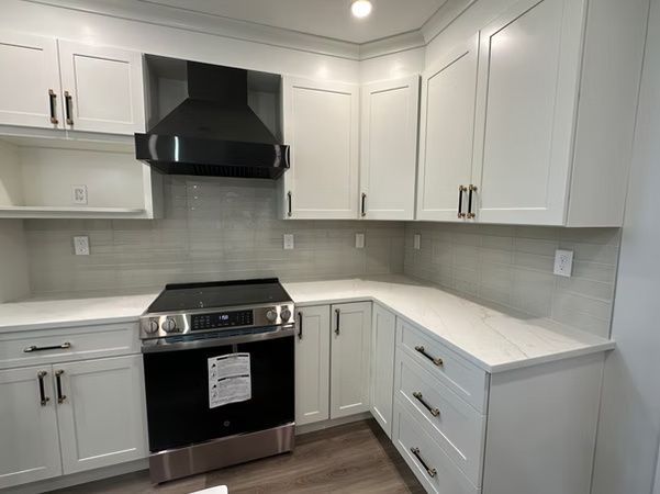 Modern white kitchen with black stove and hood, white cabinets, and light countertops