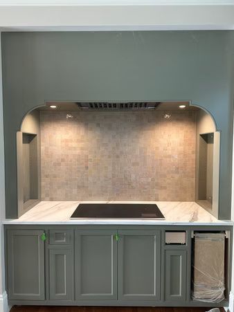 Built-in kitchen cooktop alcove with gray cabinets, marble backsplash, and under-cabinet lighting