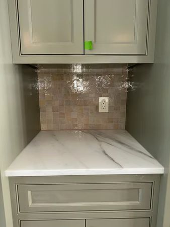 Built-in desk nook with gray cabinets, marble-look countertop, tile backsplash, and wall outlet