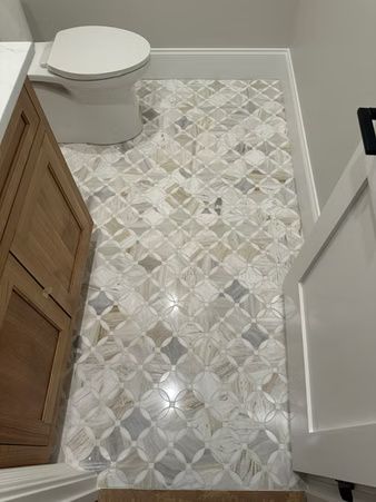 Small bathroom with patterned tile floor, white toilet, wood vanity, and open door.