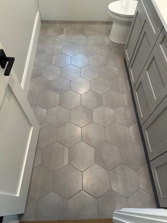 Gray hex tile bathroom floor with a toilet at the far end and cabinets along the side