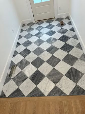 Hallway floor with black, white, and gray diamond-pattern tile, bordered by wood flooring near a door