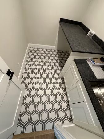 Narrow kitchen with patterned tile floor, white cabinets, and dark countertops, viewed from above