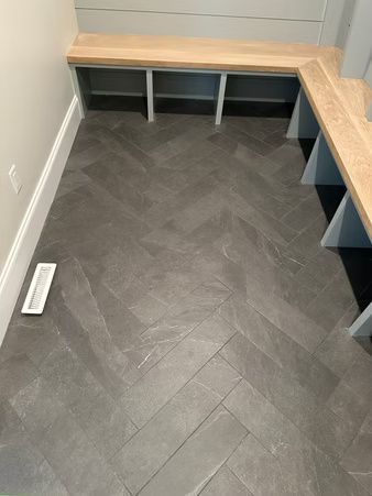 L-shaped built-in bench with wood top and gray cubbies in a small room with dark herringbone floor