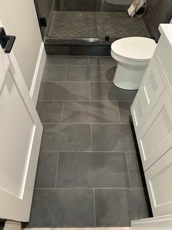Narrow bathroom with gray tile floor, white doors, and a toilet beside a walk-in shower.