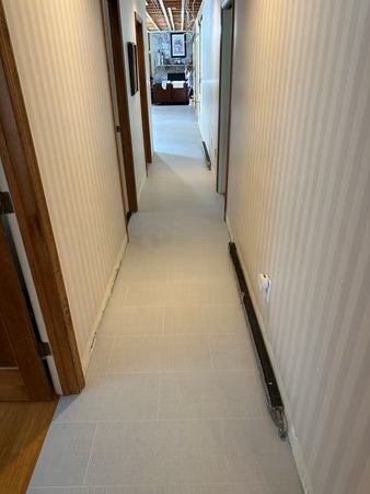 Narrow hallway with beige walls and tiled floor leading to a bright room at the end.