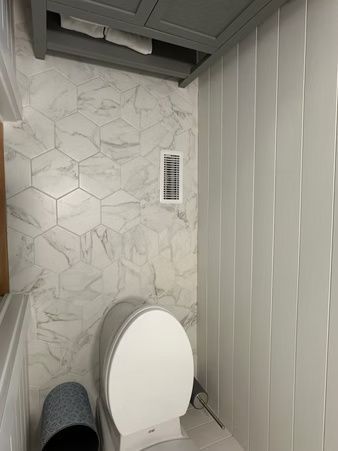 Small bathroom with white toilet, marble-pattern wall tile, and gray vertical paneling.
