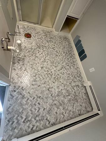 Bathroom with gray mosaic tile floor, sink, shower, and open door to a small closet.