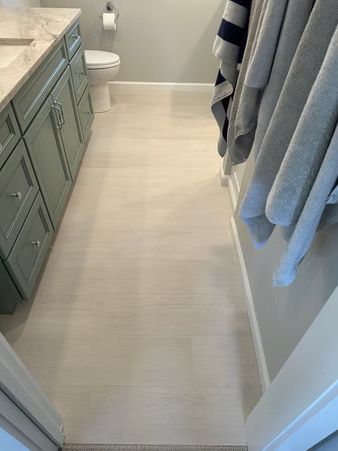 Narrow bathroom walkway with light tile floor, green vanity, white toilet, and striped towels by the shower.