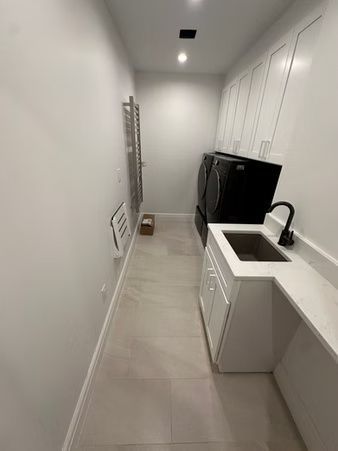Narrow modern kitchen with white cabinets, black fridge, sink, and tiled floor.