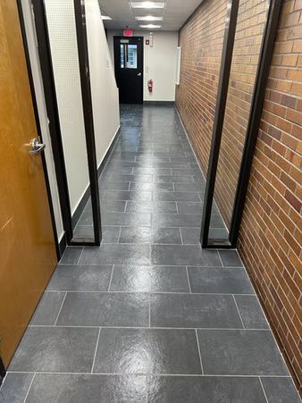 Narrow hallway with brick and white walls, dark tile floor, and doors along the sides.