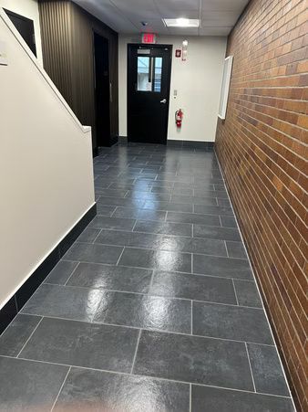 Empty hallway with dark tile floor, brick wall, and a door at the far end