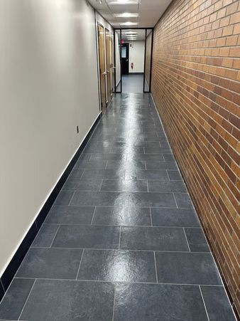 Narrow hallway with dark tile floor, white wall on one side and brick wall on the other.
