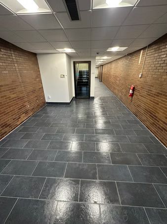 Empty hallway with brick walls, dark tiled floor, white ceiling, and a fire extinguisher on the right.