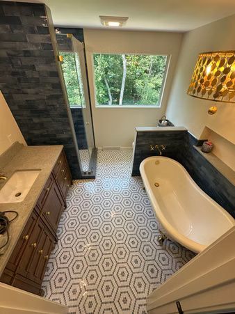 Bathroom with hexagon tile floor, freestanding tub, dark vanity, and large window overlooking greenery