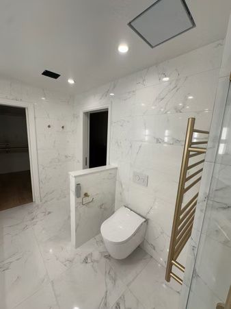 Bright white modern bathroom with toilet, marble walls, and gold towel rack