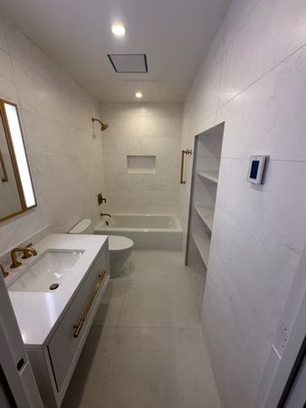 Modern bathroom with white sink vanity, toilet, bathtub, and built-in shelves on tiled walls.