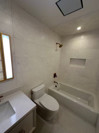 Modern white bathroom with toilet, vanity sink, and built-in tub-shower.